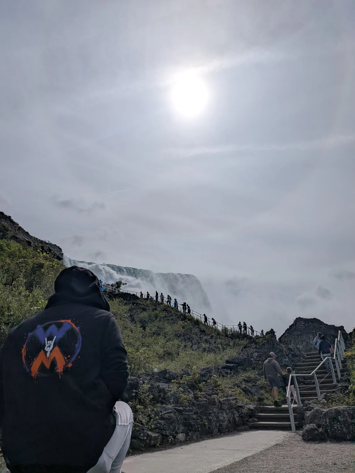 Person wearing a Worth More Movement hoodie on a rocky trail beside a waterfall